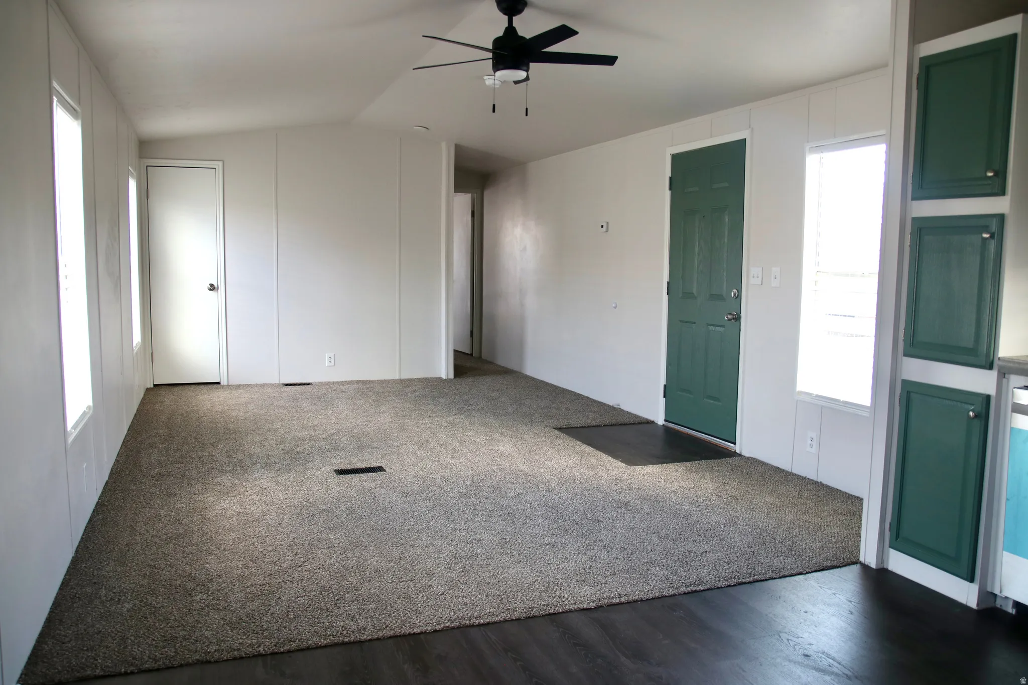 Spacious living area featuring neutral carpeting, dark wood-finish flooring, and a ceiling fan