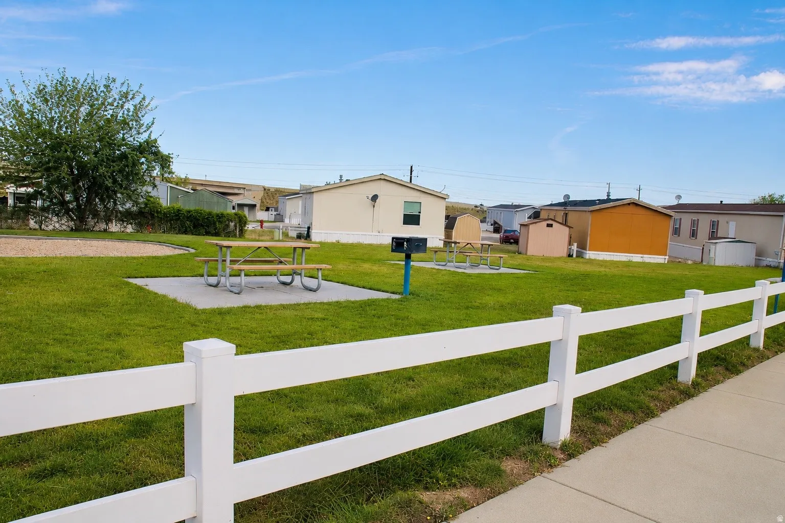 Expansive green space featuring a picnic area with multiple tables, a dedicated grilling station, and a white picket fence border