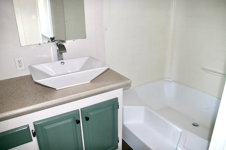 Primary Bathroom featuring a vessel sink, single-lever faucet, vanity with green cabinetry, a solid surface countertop, and a white tub with tiled surround