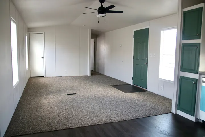 Spacious living area featuring neutral carpeting, dark wood-finish flooring, and a ceiling fan