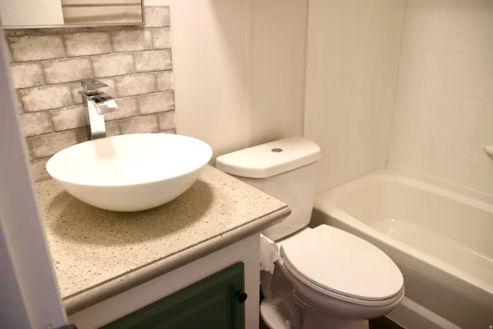 Guest bathroom featuring Vessel sink with a chrome waterfall faucet, brick-patterned tile backsplash, and a contemporary toilet