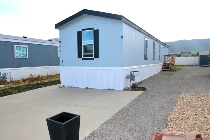 Light blue siding with new white skirting, dark roof, dark shutters, and a concrete driveway
