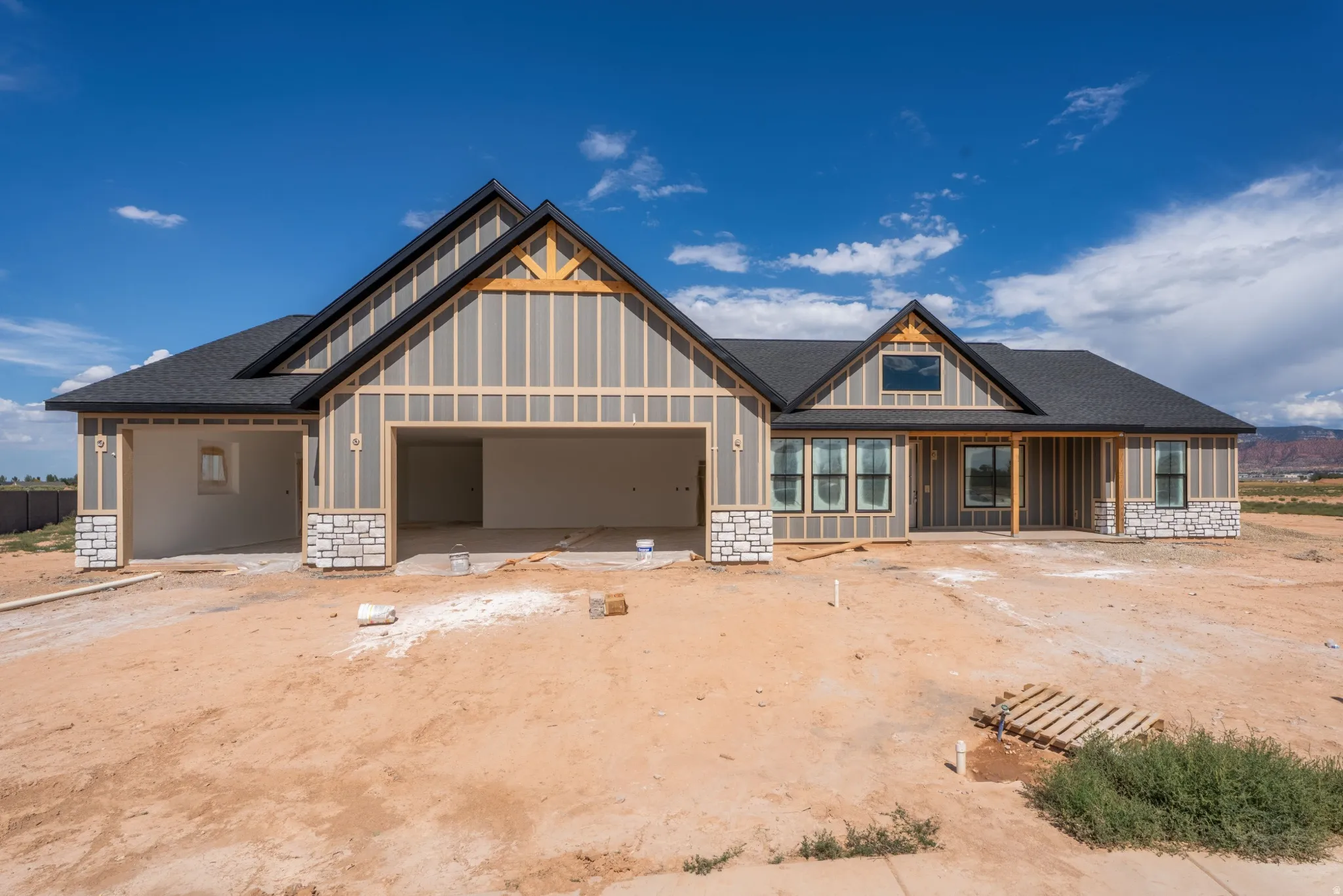 Contemporary farmhouse-style exterior featuring board and batten siding, stone veneer accents, an exposed timber gable truss, and a dark shingle roof