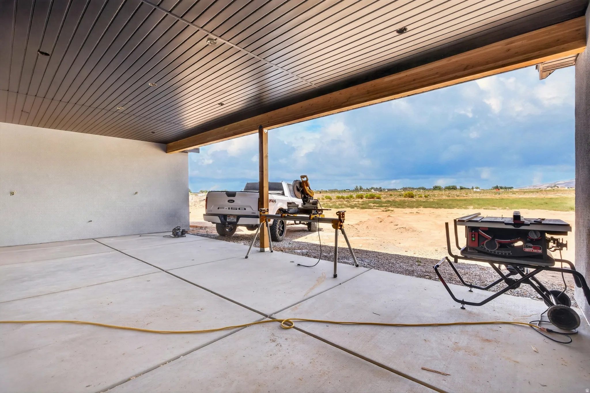 Concrete patio with an exposed beam, a metal plank ceiling, and a distant field