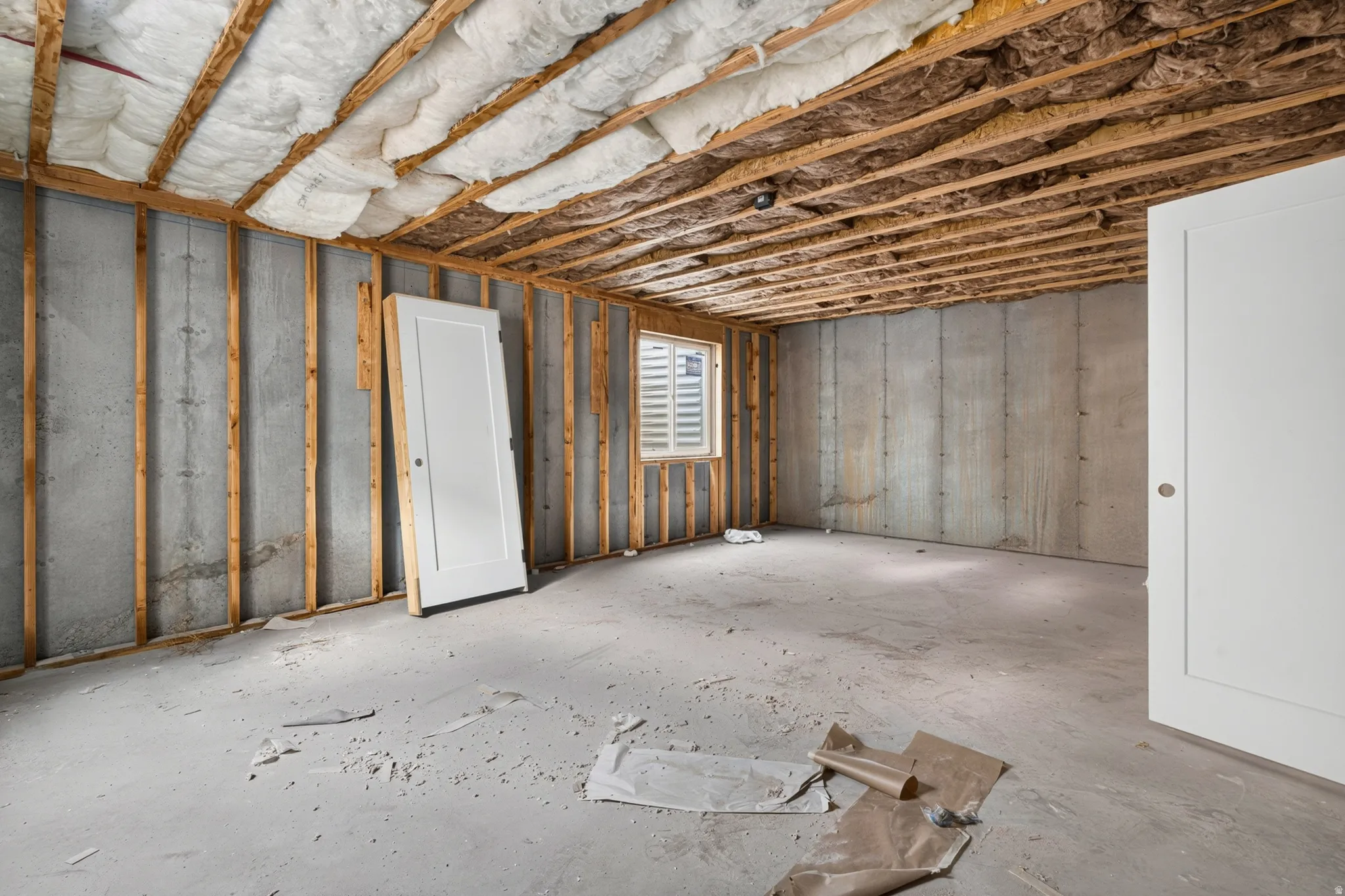 Concrete foundation walls with wood framing, exposed ceiling joists, and a window with horizontal blinds