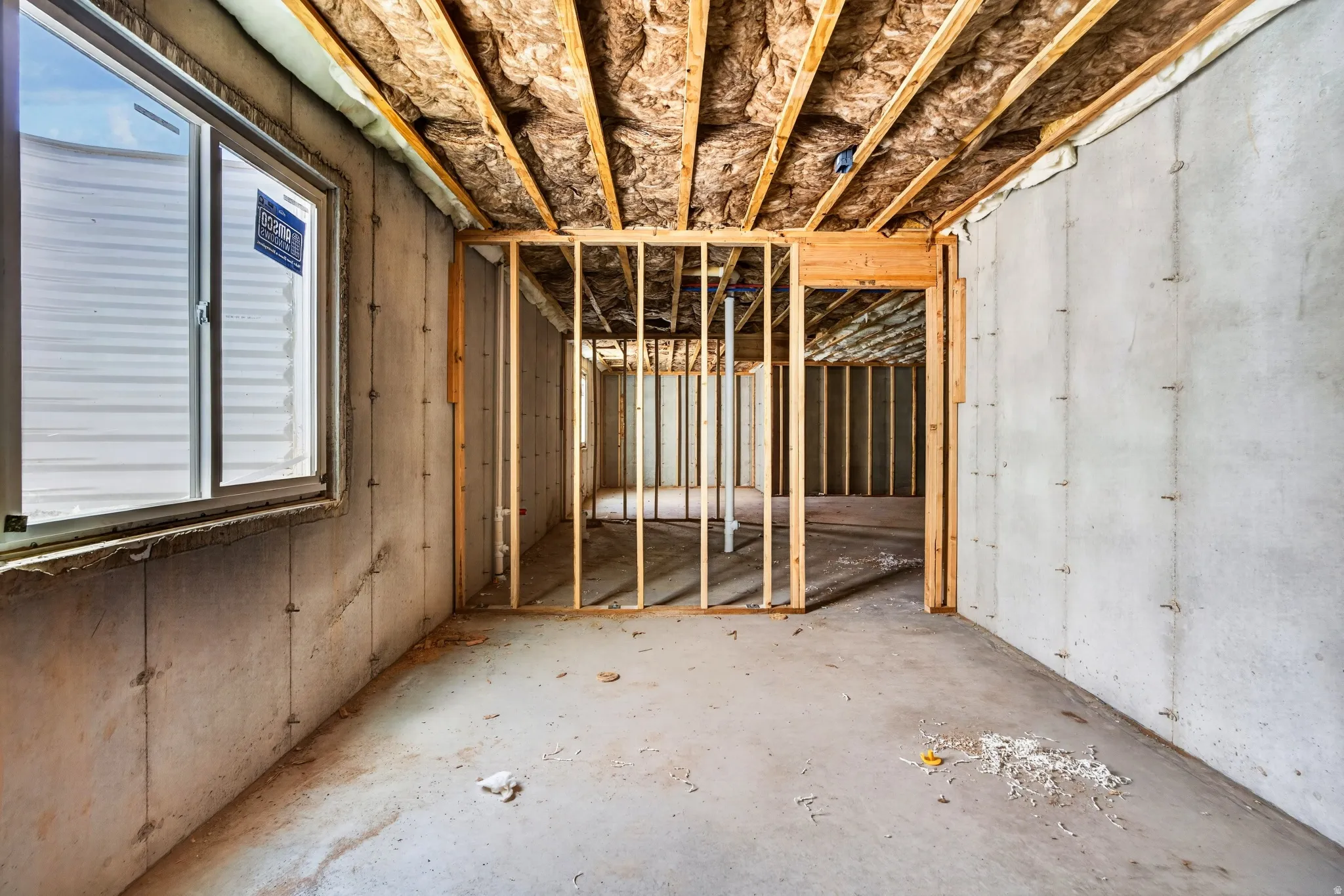 Unfinished lower level featuring concrete walls, an egress window, wood framing, and exposed insulation