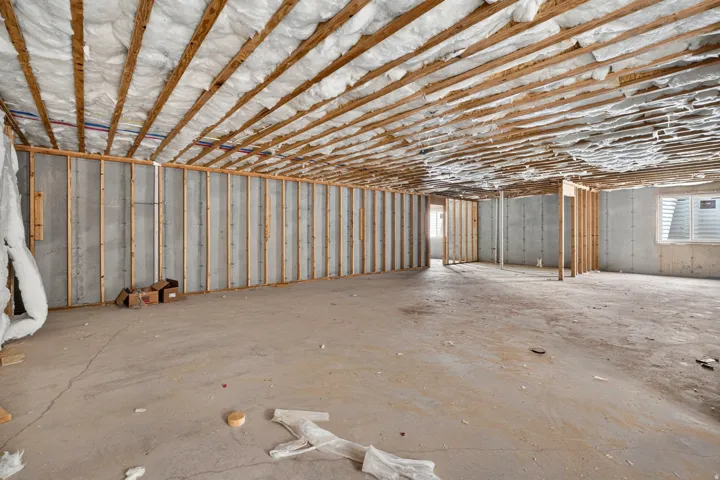 Unfinished basement featuring concrete walls, exposed wood framing, concrete flooring, and an egress window