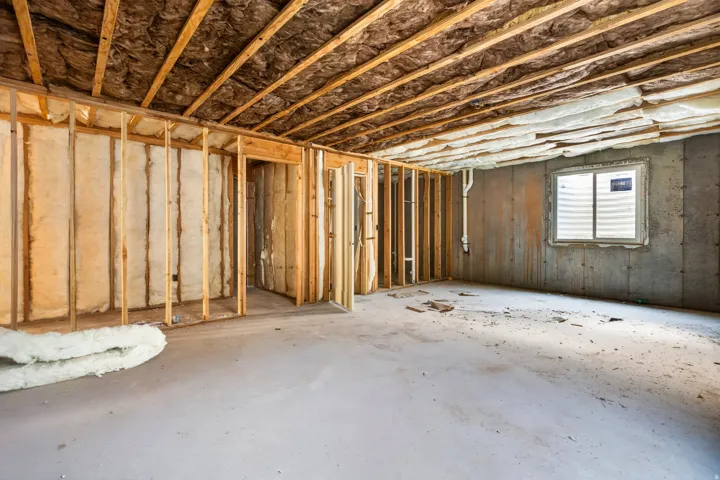 Unfinished basement featuring wood framing, concrete foundation walls, exposed ceiling joists, and a window well