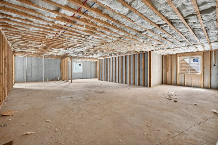 Expansive unfinished space featuring insulation, exposed ceiling joists, wood wall framing, and concrete flooring