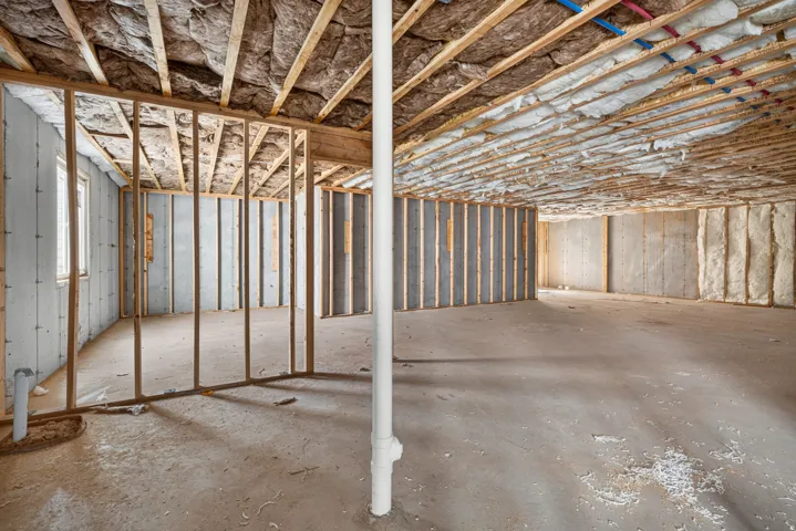 Unfinished basement with concrete slab flooring, wood framing, exposed joists with insulation, and concrete foundation walls