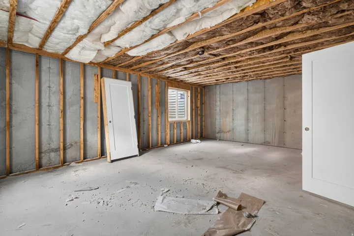 Concrete foundation walls with wood framing, exposed ceiling joists, and a window with horizontal blinds