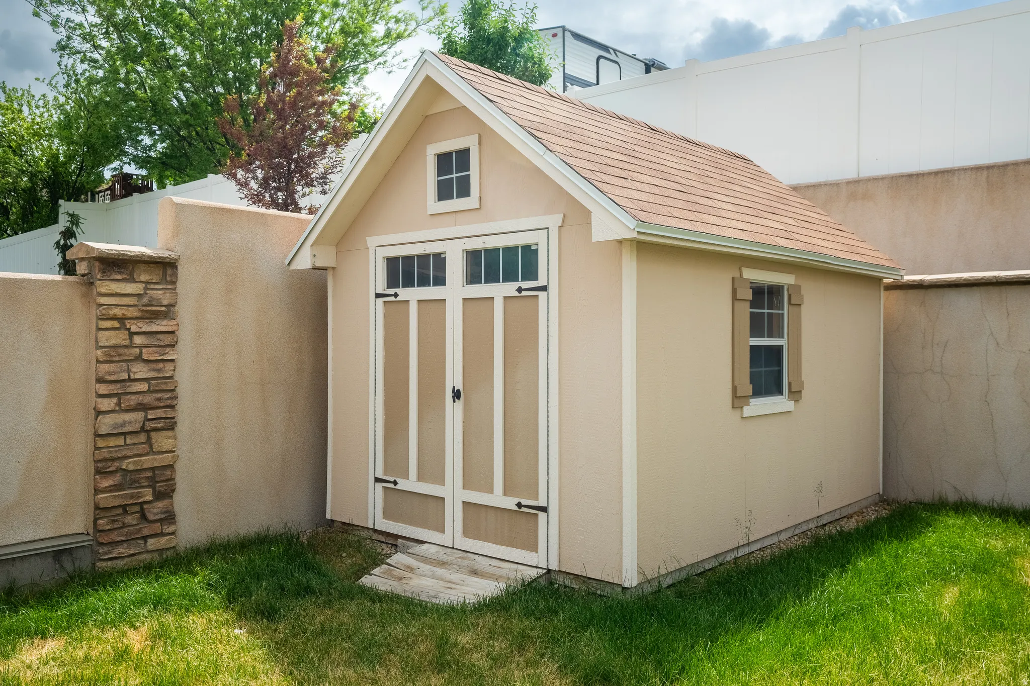 Gable-roofed storage shed with a light-colored exterior, double barn-style doors, and decorative windows