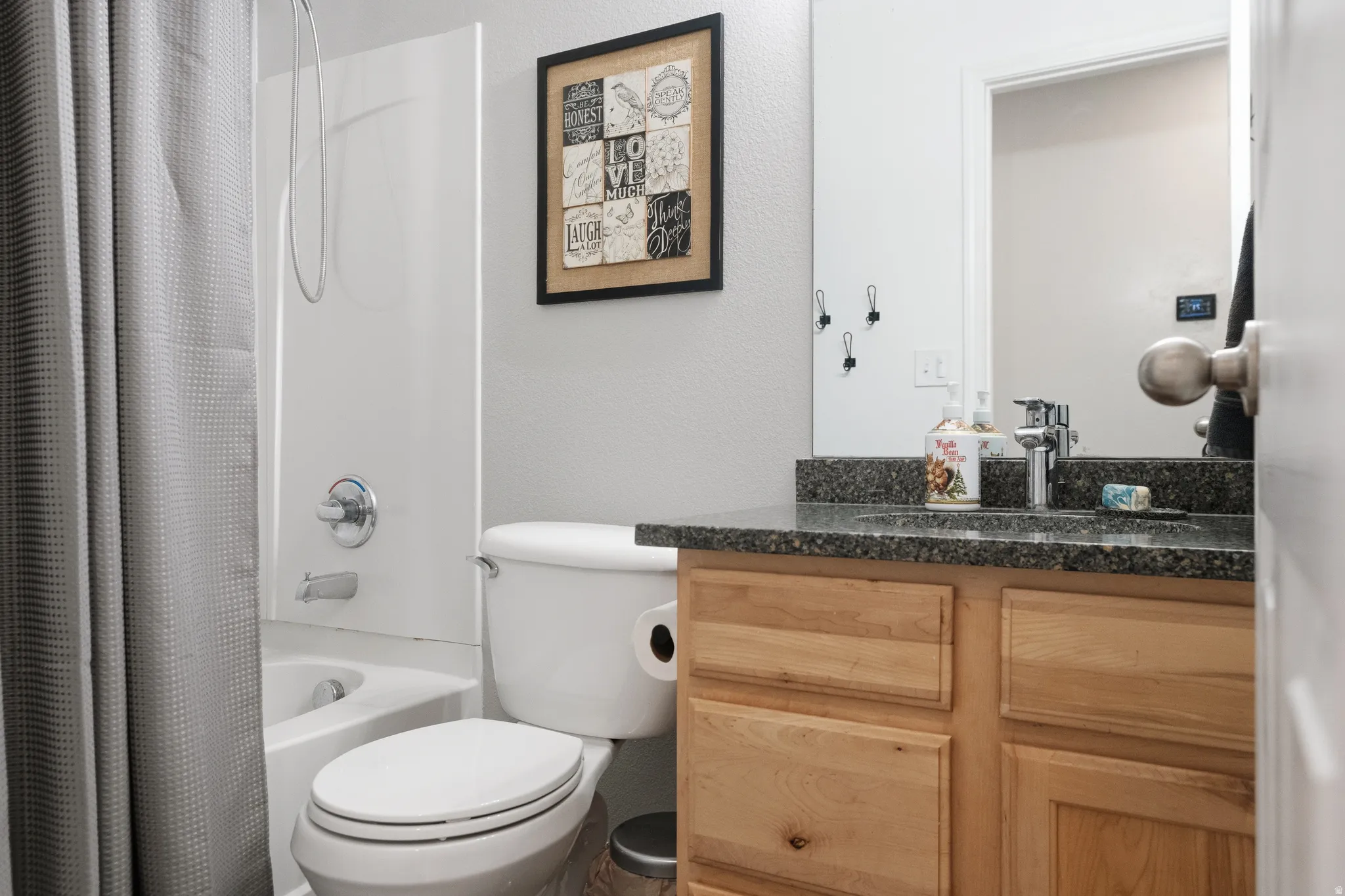 Bathroom featuring a single-sink vanity with wood-finish cabinetry, a dark speckled countertop, and a chrome faucet