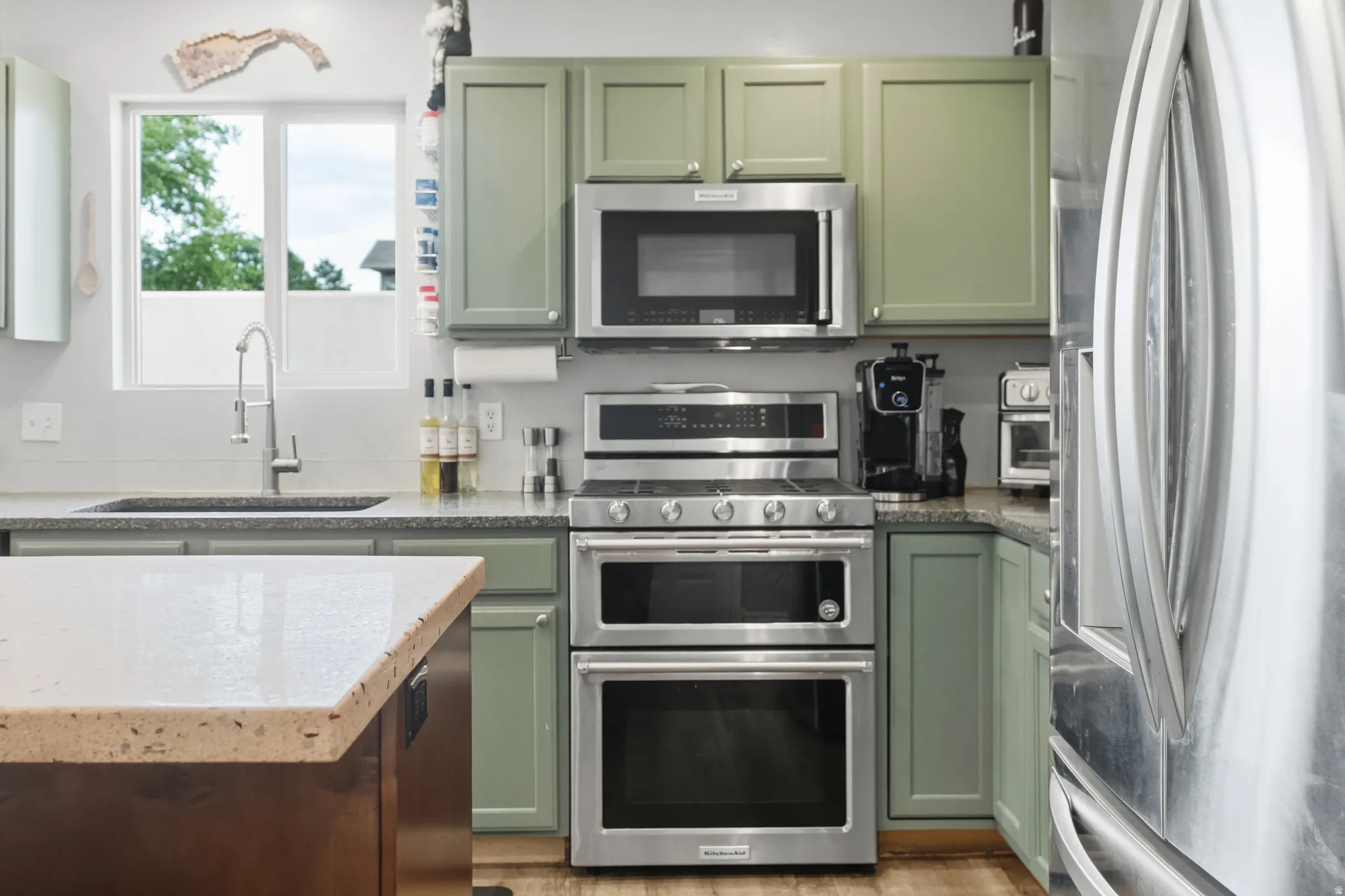 Kitchen featuring sage green cabinetry, stainless steel appliances, a double oven range, and light-toned countertops