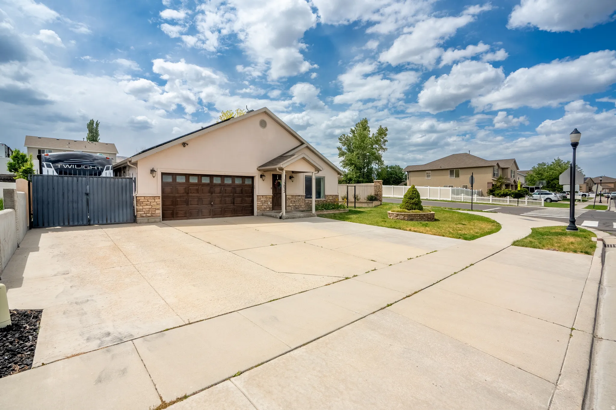 Front exterior featuring a stucco facade, stone accents, a two-car garage with wood-finish door, a concrete driveway, and a gated side yard