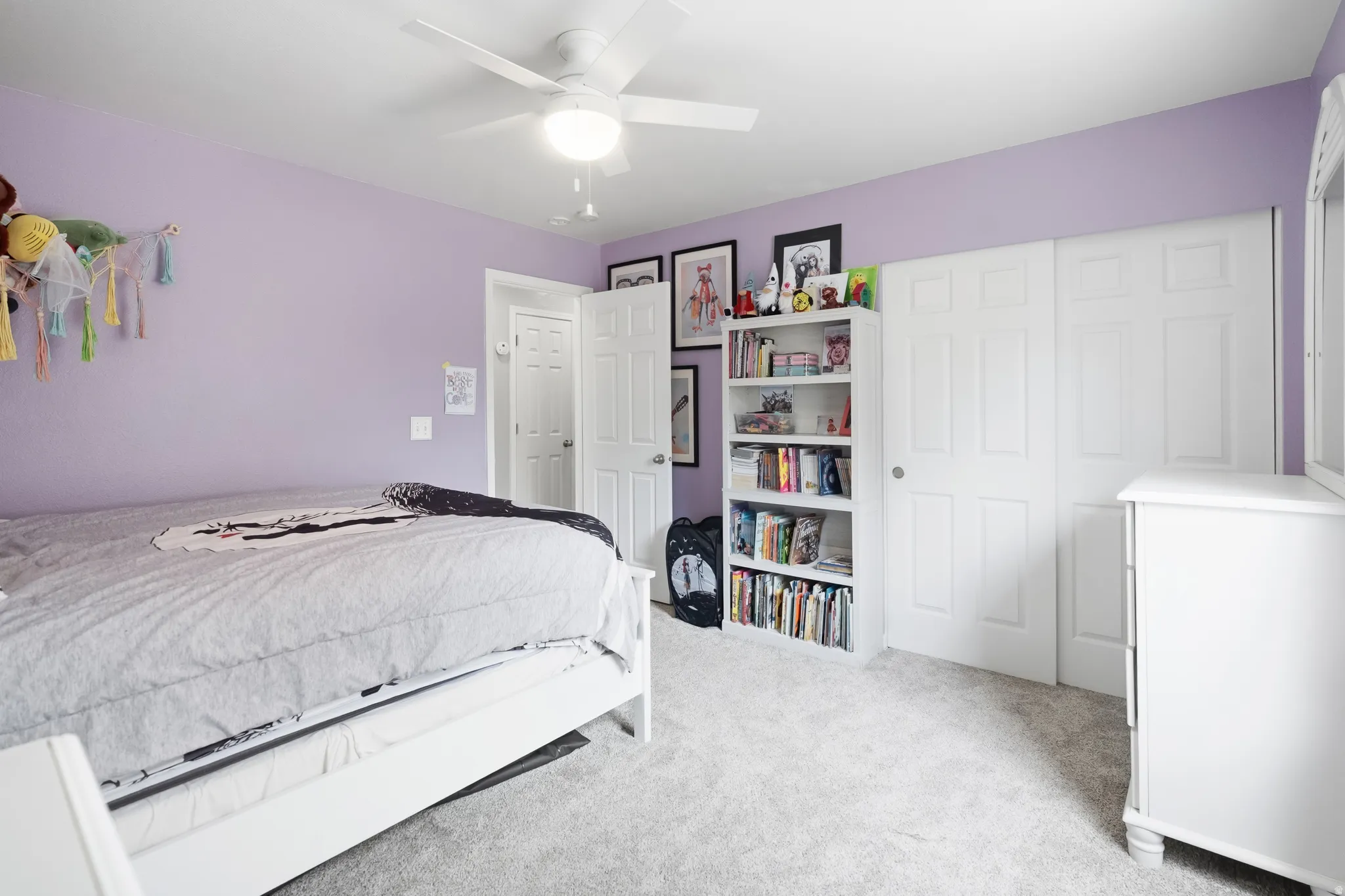 Bedroom featuring a ceiling fan with integrated lighting, two panel-style closet doors, a white built-in shelving unit, and wall-to-wall carpeting