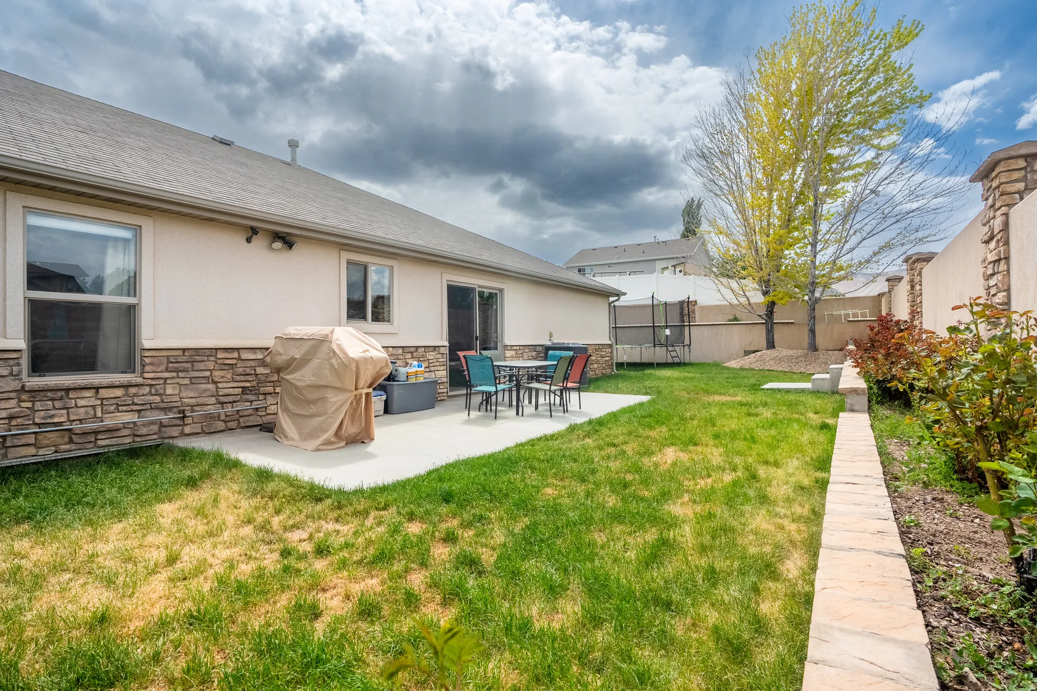 Expansive private yard featuring a concrete patio, mature trees, and a stone-clad perimeter wall