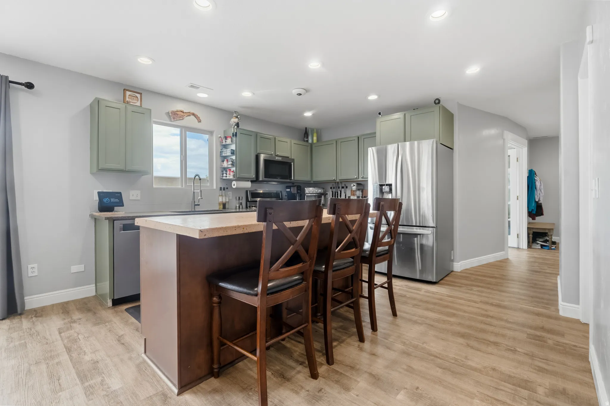 Kitchen featuring an island with seating, stainless steel appliances, light green cabinetry, recessed lighting, and wood-finish flooring