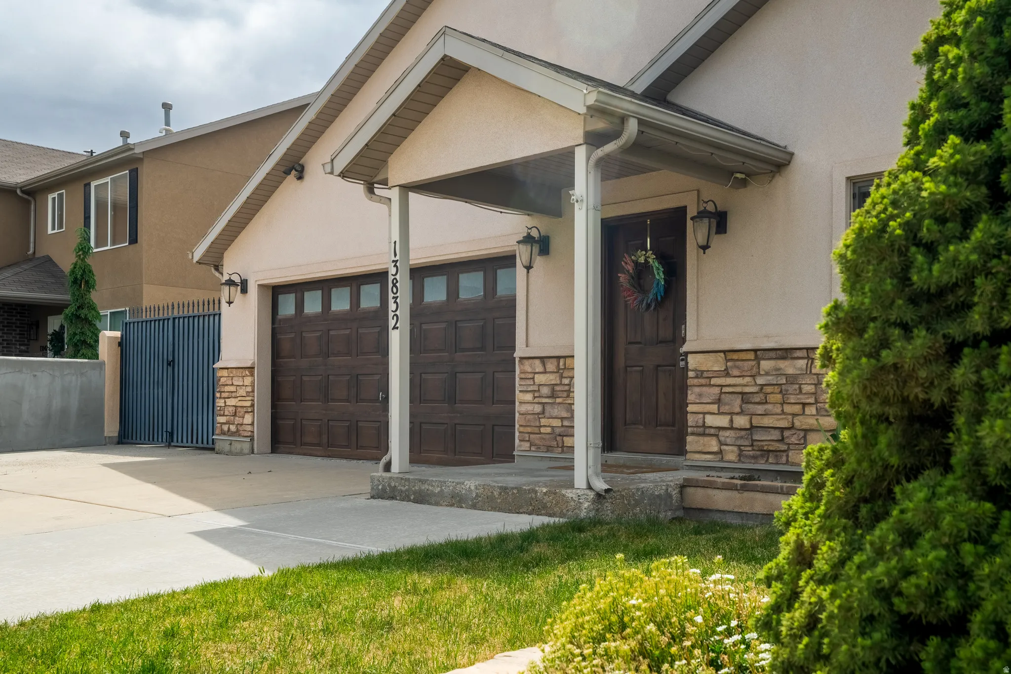 Stucco exterior with stone veneer accents, concrete driveway, two-car garage with paneled doors, covered entry, and established perimeter plantings