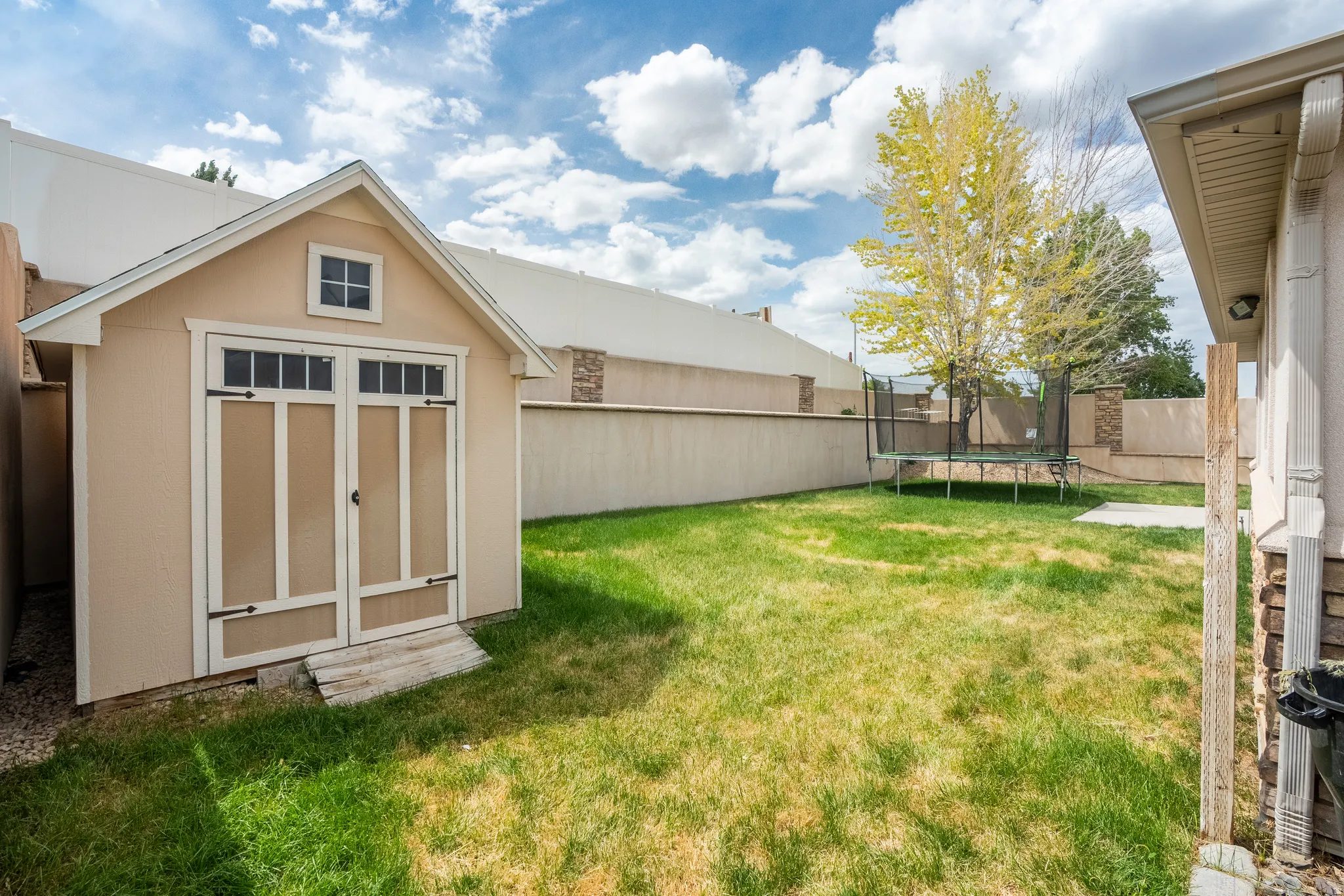 Spacious backyard featuring a storage shed with double doors, mature trees, a concrete patio area, and perimeter fencing