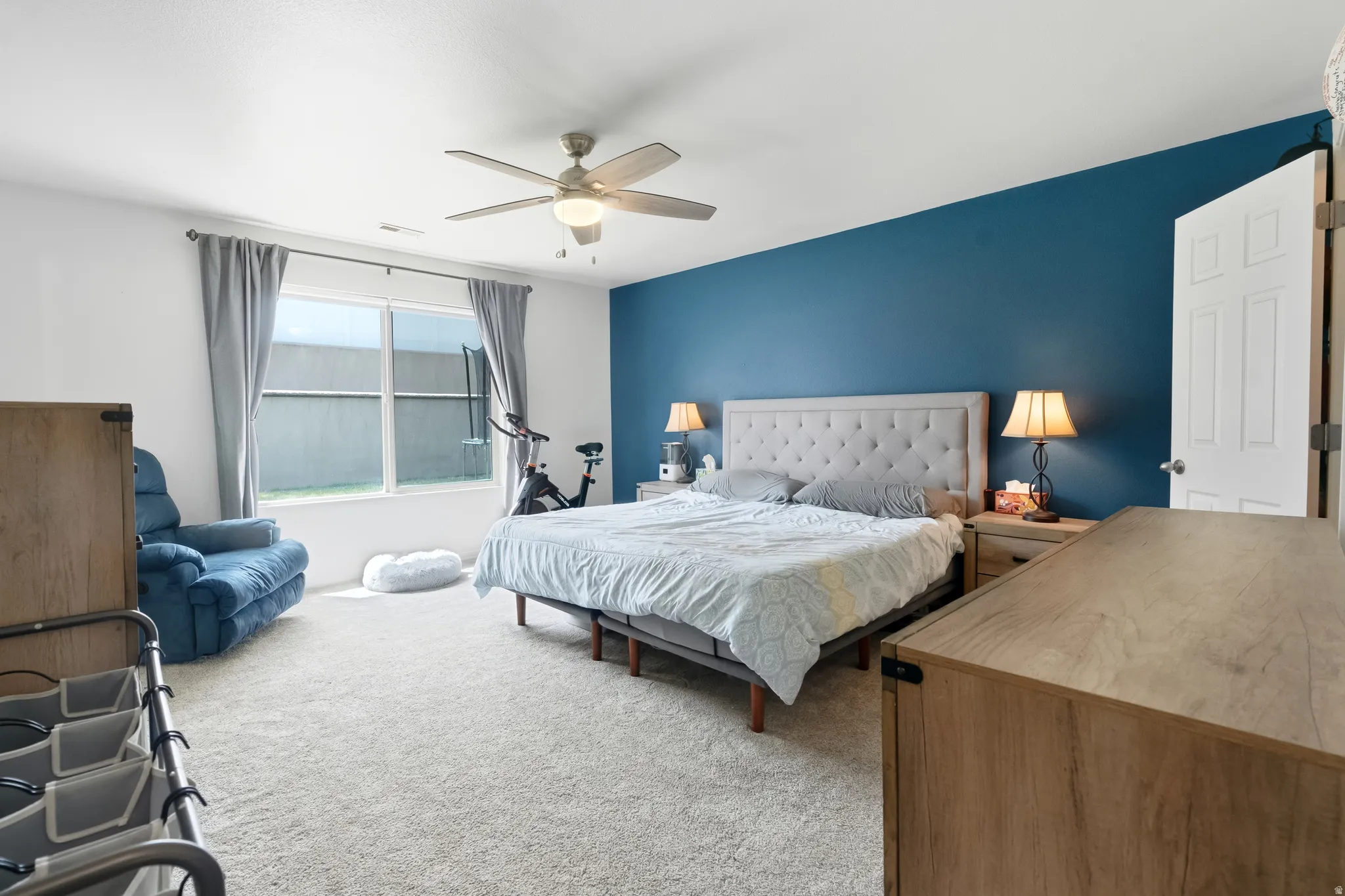 Spacious bedroom featuring light-toned carpeting, a ceiling fan, and a large window overlooking the exterior