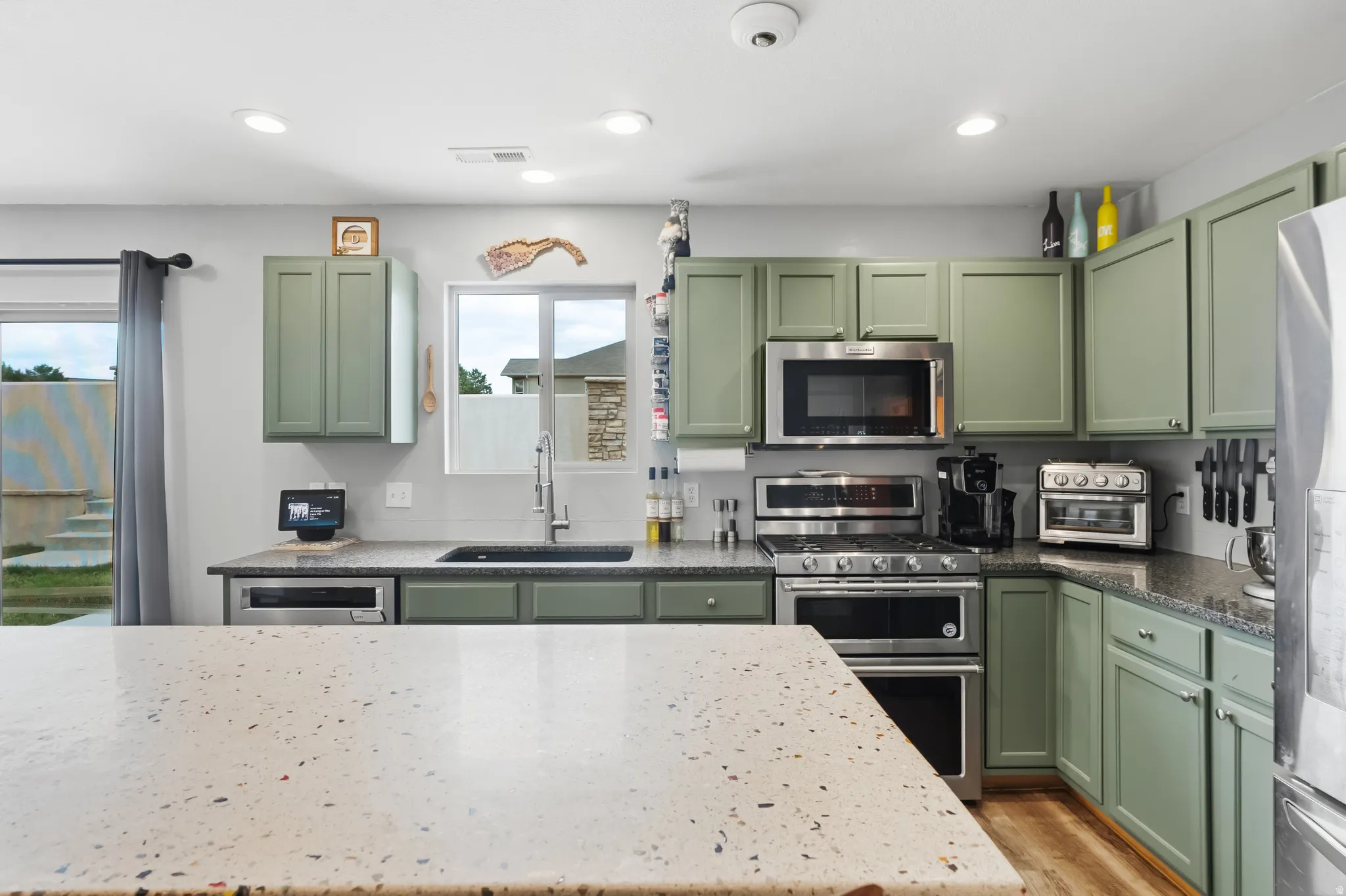 Kitchen with light green cabinetry, stainless steel appliances, and a light-toned speckled countertop