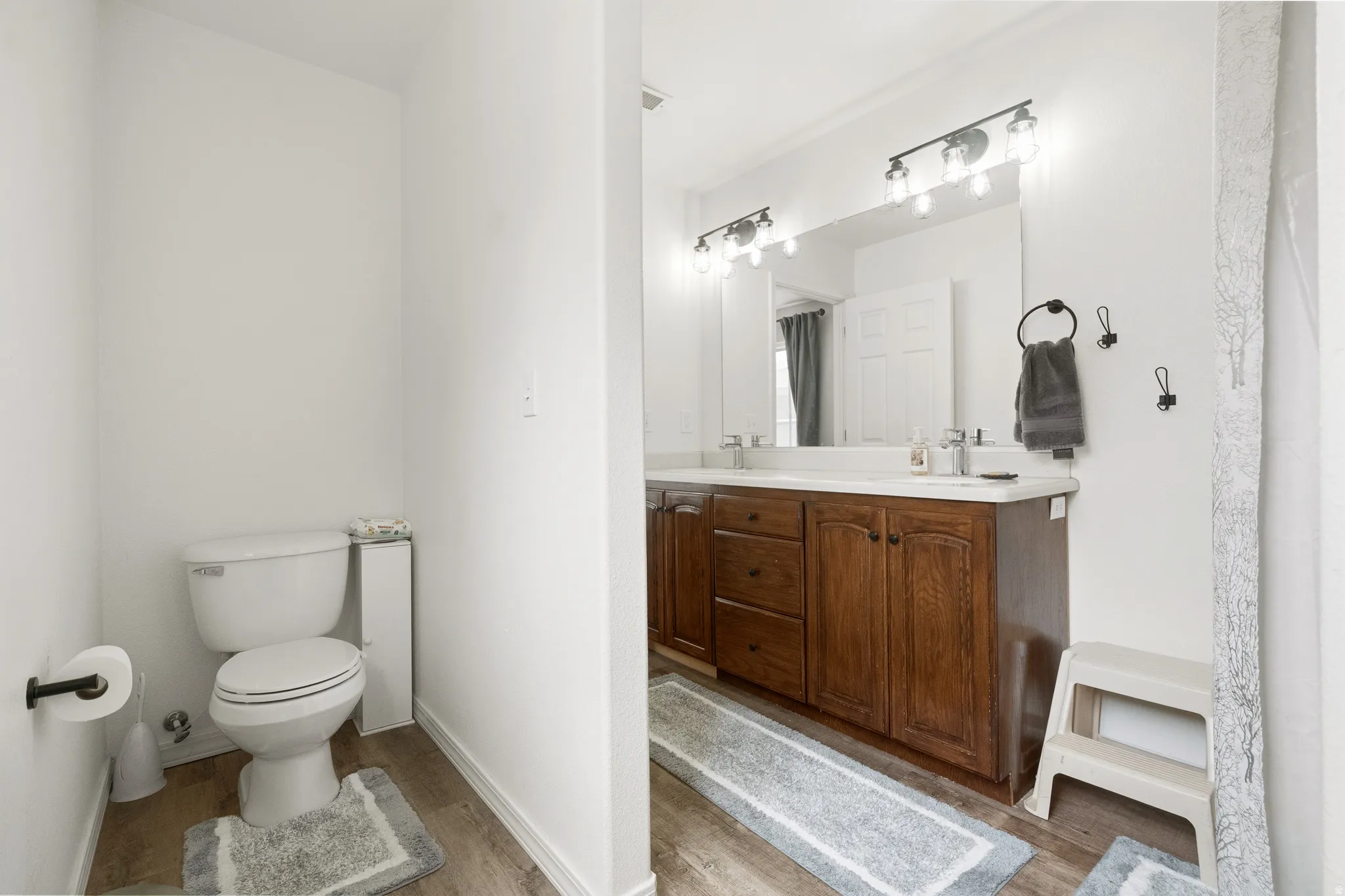 Bathroom featuring a double vanity with wood-finish cabinetry, a large integrated mirror, and dual light fixtures