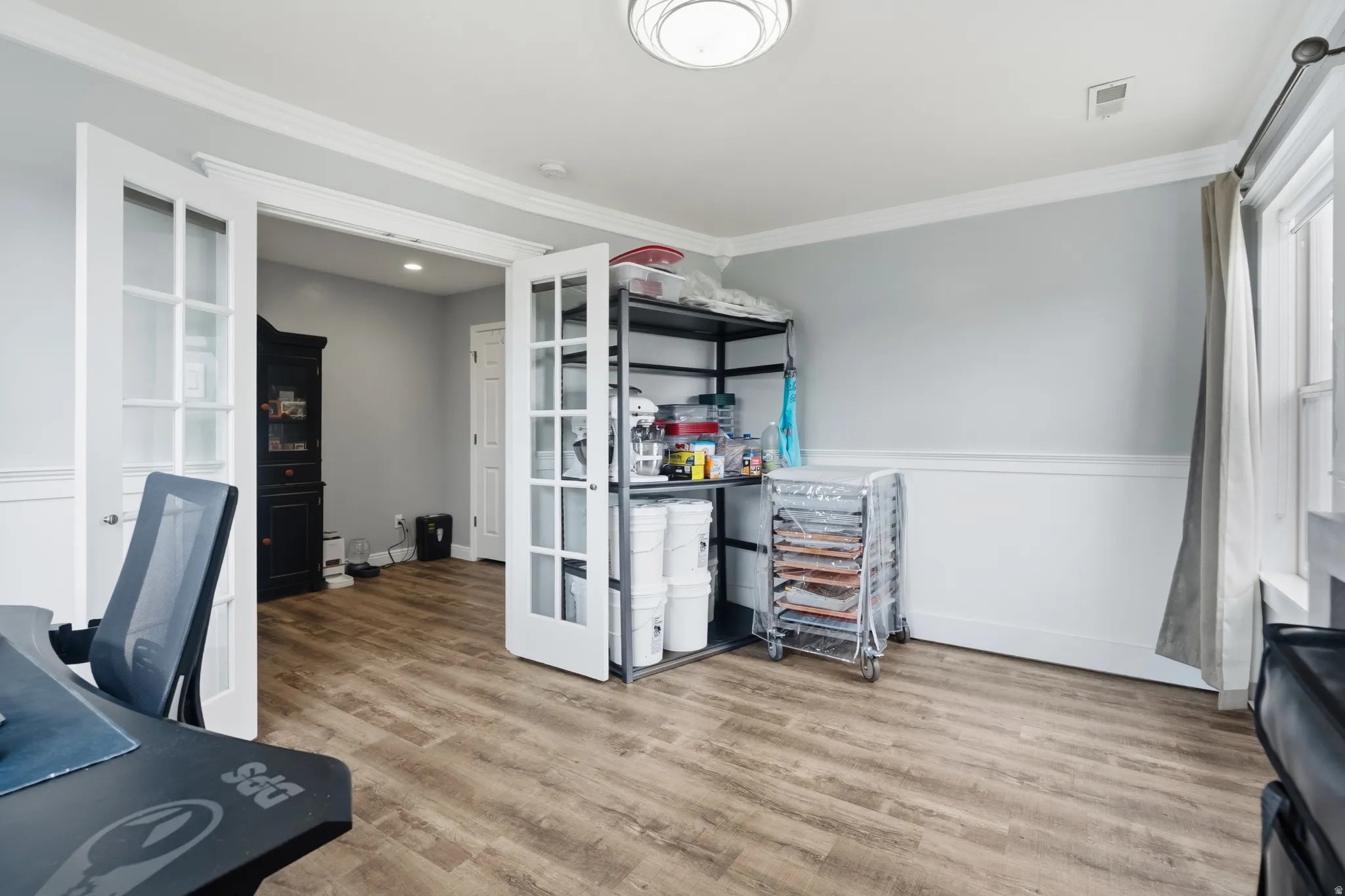 Room featuring wood-finish flooring, white paneled wainscoting, and crown molding