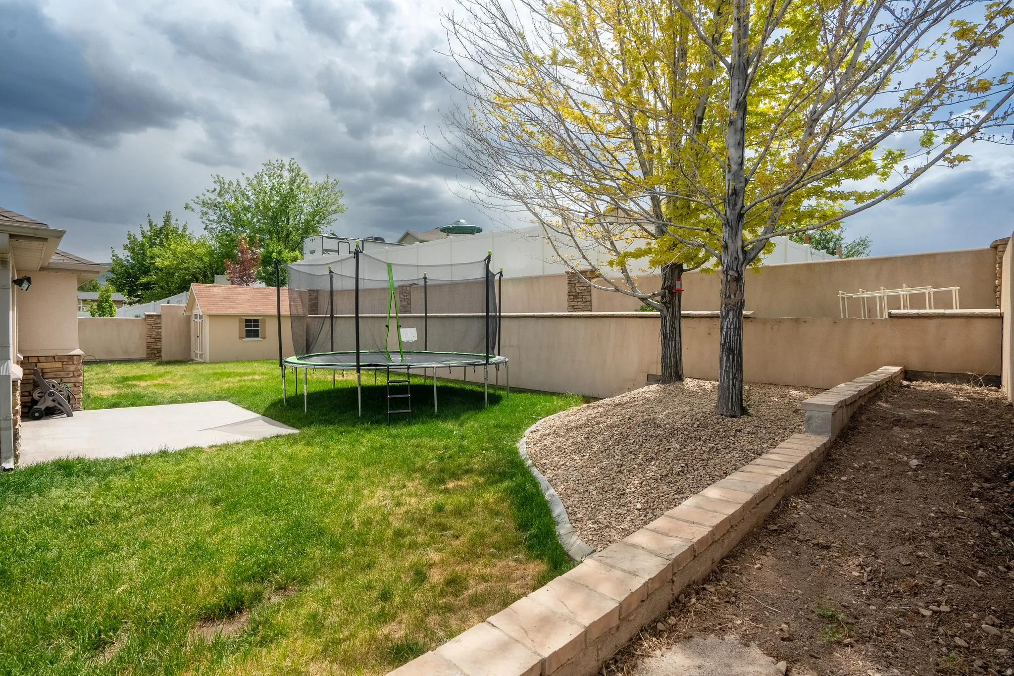 Expansive backyard featuring a concrete patio, grassy lawn, mature trees, and a storage shed