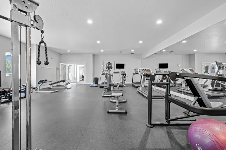 Spacious fitness center featuring rubber flooring, recessed lighting, mirrored walls, and double glass doors