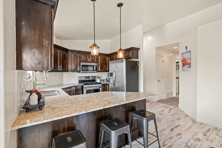 Kitchen featuring dark wood cabinetry, light-toned granite countertops, stainless steel appliances, a tile backsplash, and light wood-finish flooring