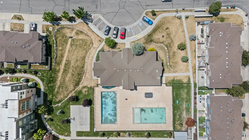 Community amenities featuring two swimming pools, a central building with a brown shingle roof, a designated parking area, and landscaped green spaces with established trees