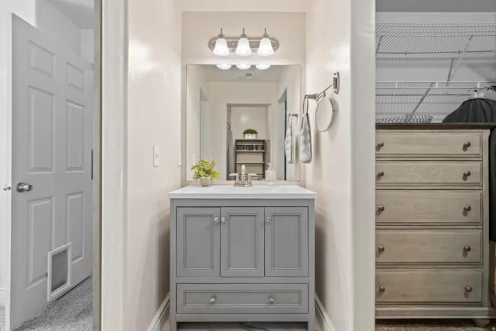 Modern vanity featuring a gray cabinet with double doors and a bottom drawer, white countertop with an integrated sink, and an overhead three-light fixture