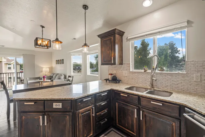 Kitchen featuring granite countertops, dark wood cabinetry, a double basin sink, and a white subway tile backsplash