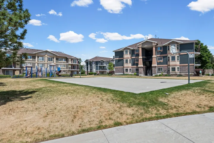 Basketball court with a playground, surrounded by multi-story residential buildings featuring brick and siding exteriors