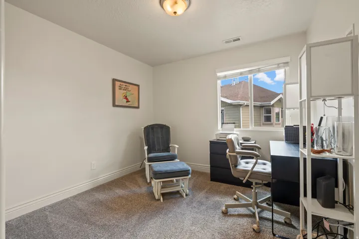 Bright interior room with a large window, light-colored walls, and gray carpeting