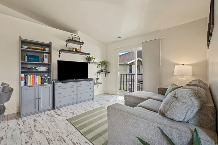 Living area featuring high vaulted ceilings, light wood-finish flooring, and a sliding glass door opening to a private balcony