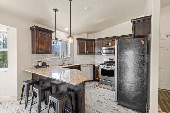 Kitchen featuring dark wood cabinetry, light-toned granite countertops, a tiled backsplash, stainless steel appliances, and wood-finish flooring
