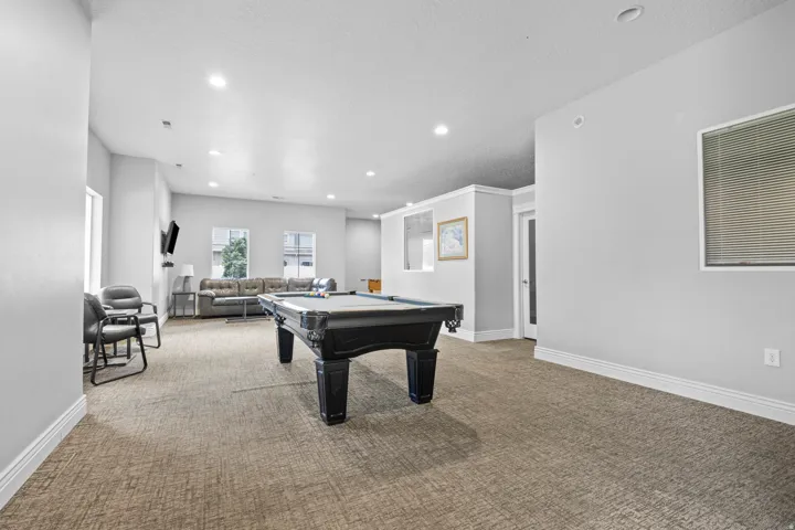 Spacious recreation room featuring recessed lighting, light-toned carpeting, white baseboards, and multiple windows with blinds