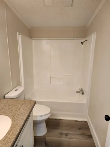 Bathroom featuring a white shower/tub combination, wood-finish flooring, a white toilet, and a vanity with a speckled countertop and integrated sink