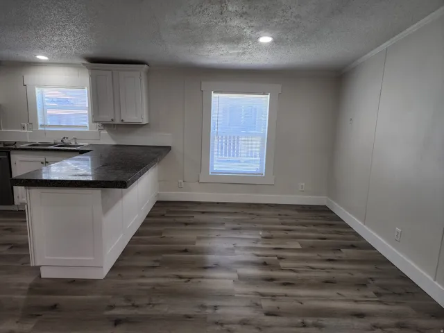 Kitchen area featuring a dark countertop island, white cabinetry, recessed lighting, and wood-finish flooring