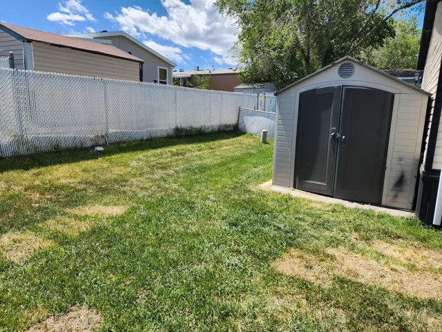 Expansive lawn area featuring a chain-link fence, a storage shed with double doors, and established greenery