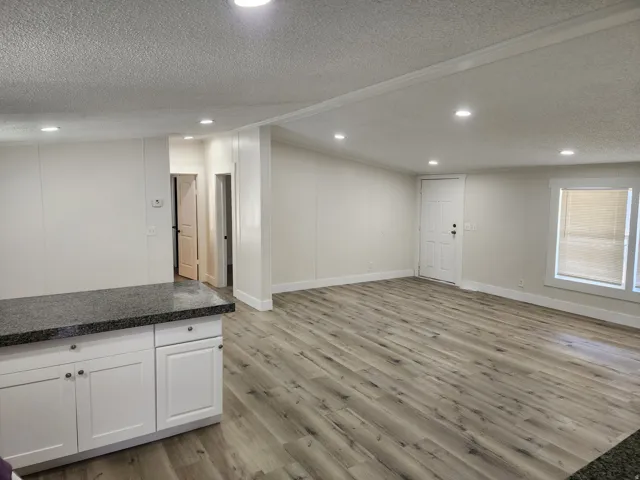 Spacious interior featuring wood-finish flooring, white paneled walls, recessed ceiling lighting, and a kitchen island with white cabinetry and a dark stone-finish countertop