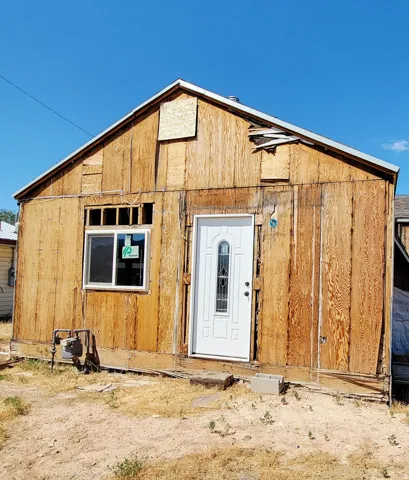 Single-story structure with exposed wood siding, a new white entry door with decorative glass, and a new white-framed window