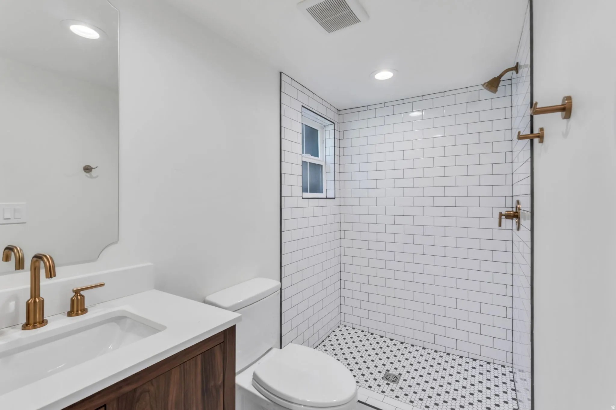 Bathroom featuring a wood-finish vanity with an integrated sink and white countertop, bronze-tone fixtures, a tiled shower with a clear glass enclosure, and recessed lighting