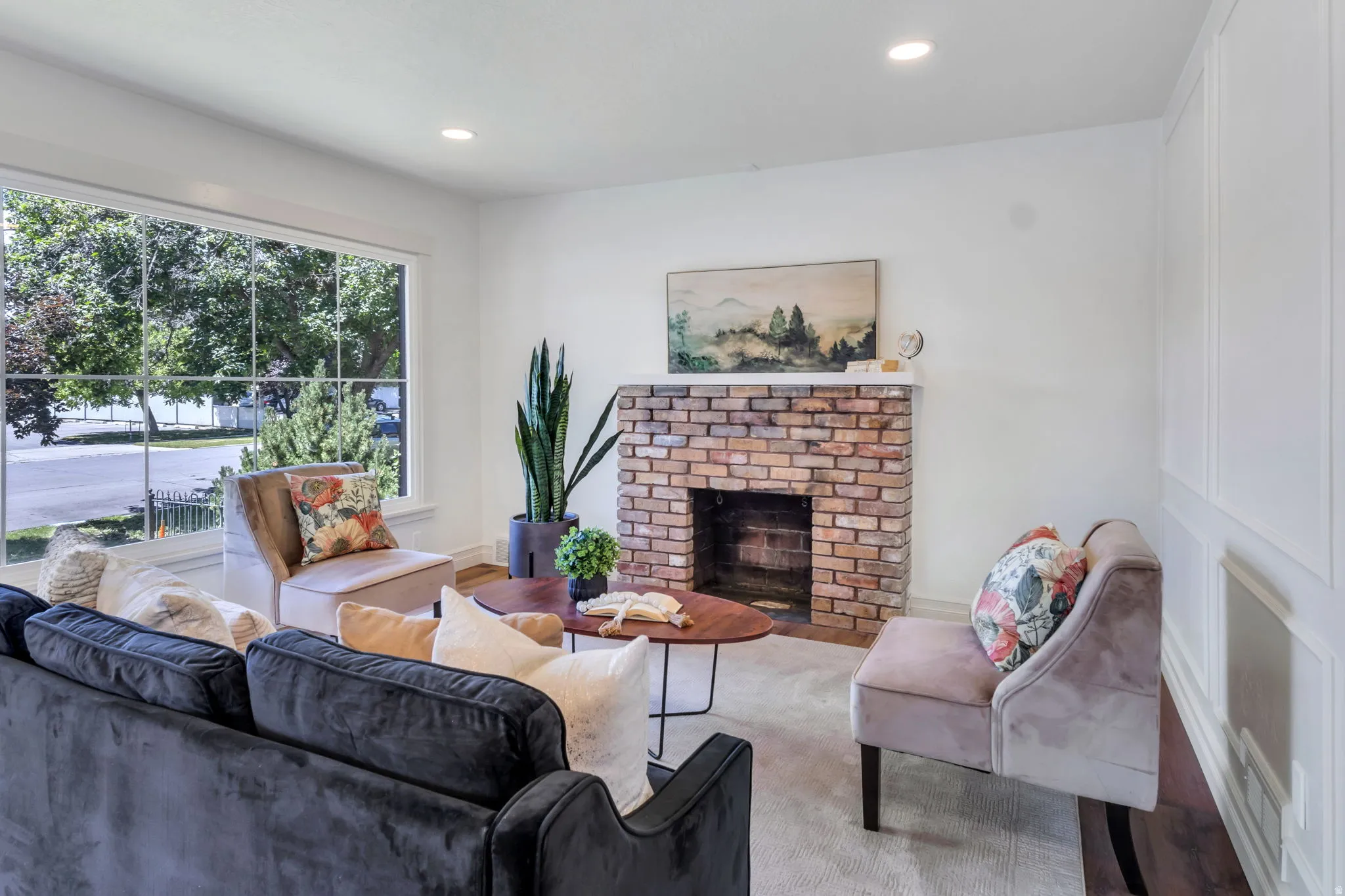 Living area featuring a brick-faced fireplace, large picture window, recessed lighting, and white paneled wall accents