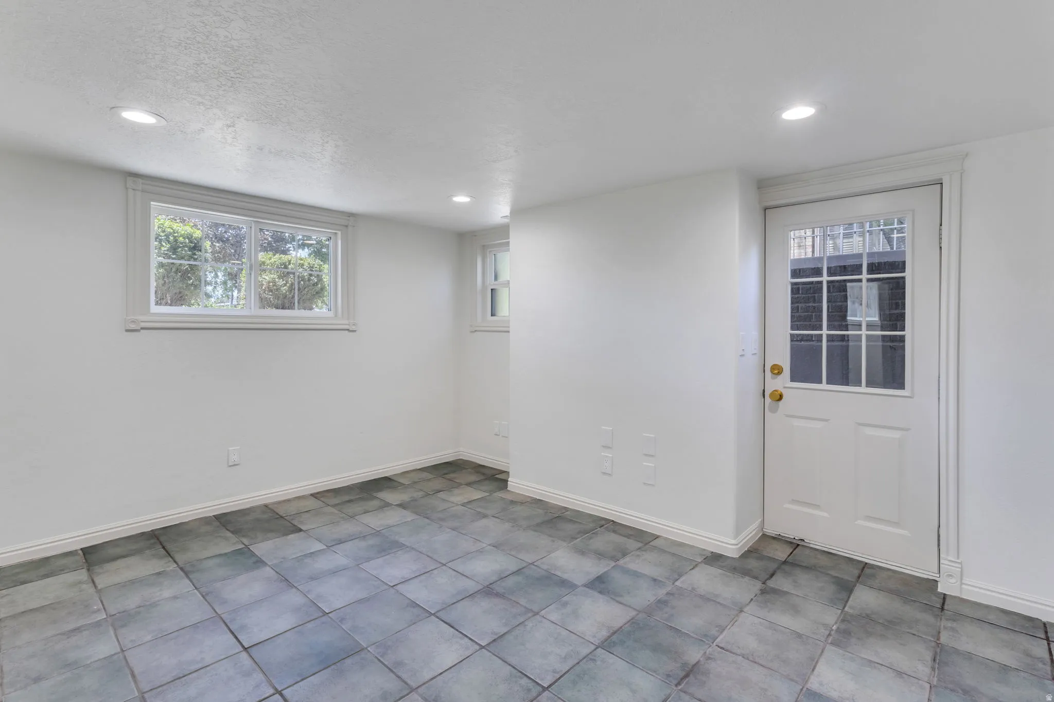 Room featuring square tile flooring, white walls, recessed lighting, and a white paneled door with glass inserts