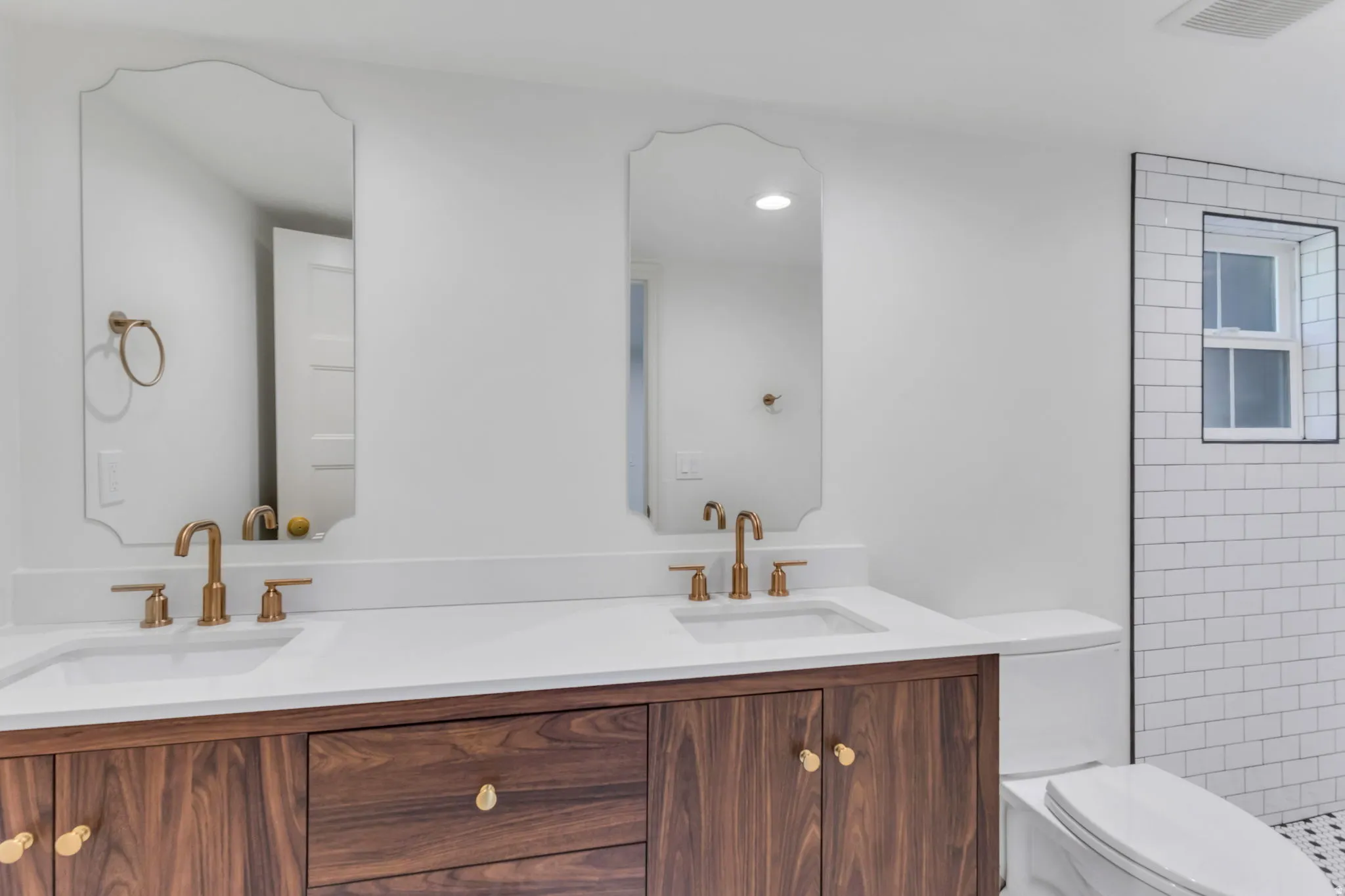 Dual vanity featuring wood-finish cabinetry, white countertops, and contemporary gold-toned fixtures