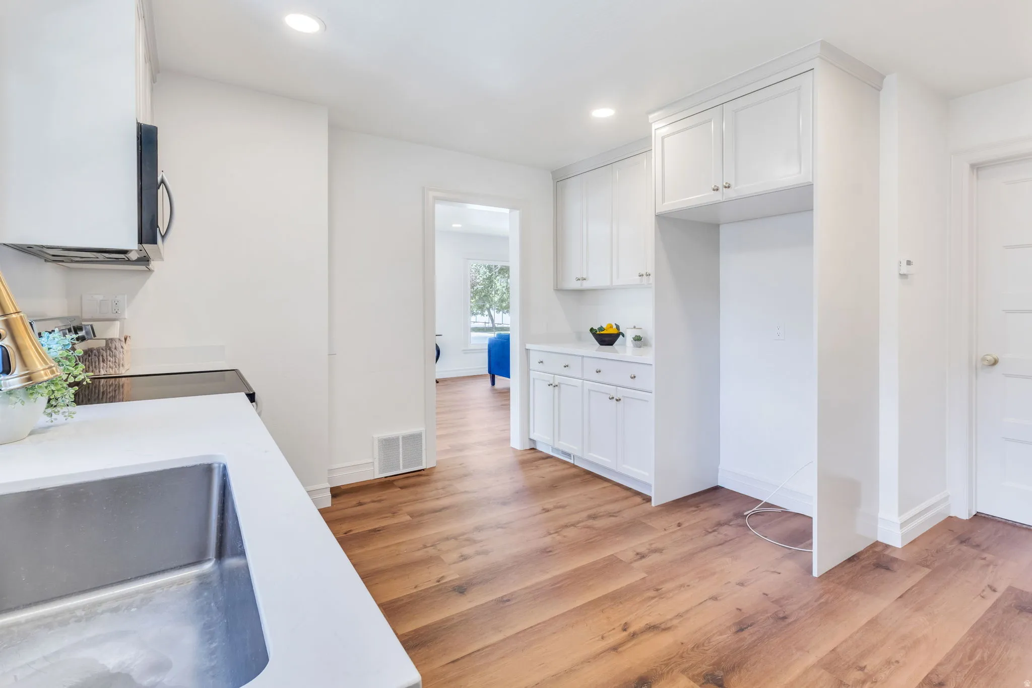 Kitchen featuring wood-finish flooring, white cabinetry with silver hardware, white countertops, and a stainless steel undermount sink