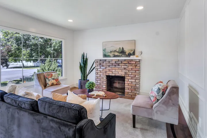 Living area featuring a brick-faced fireplace, large picture window, recessed lighting, and white paneled wall accents